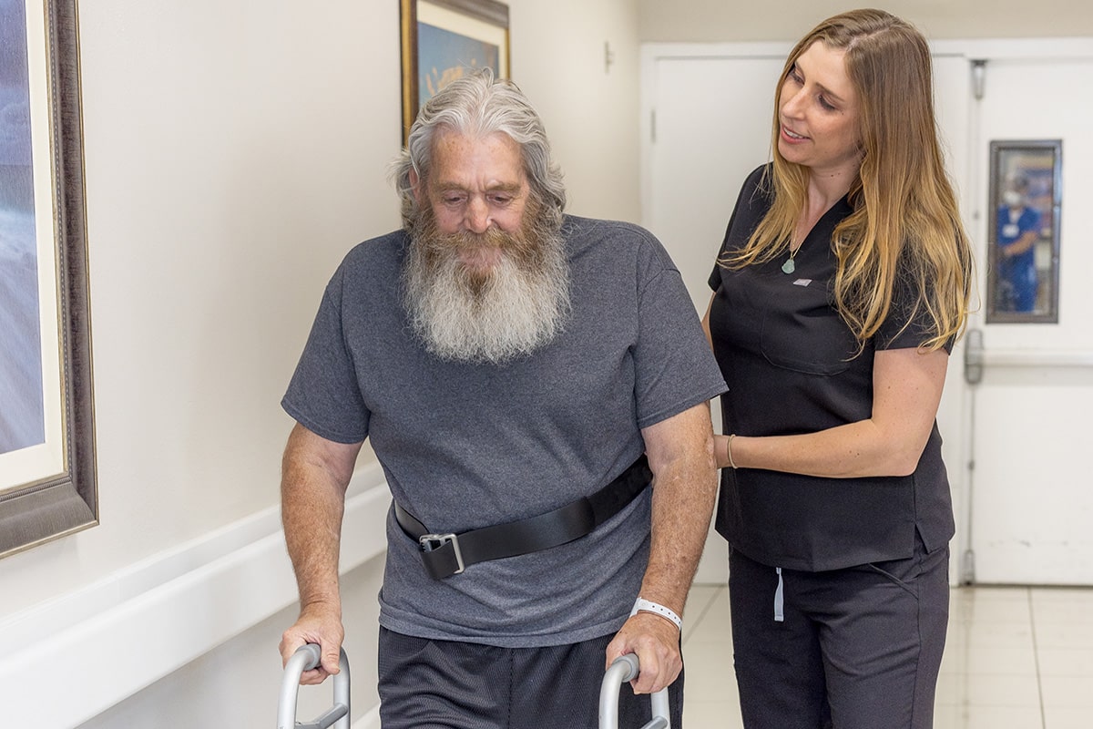a caregiver walking with a resident in the hallway at Country Hills facility